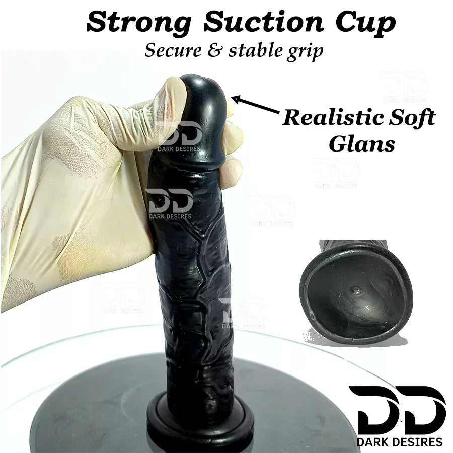 Black realistic dildo with textured details and soft glans, held by a beige nitrile glove on a  9 inch realistic strapon dildo with adjustable harness kit for  for pegging . Lifelike veins, black tone, soft glans.  Black faux leather belt Sex Toys for Women in Mumbai India by DarkDesires